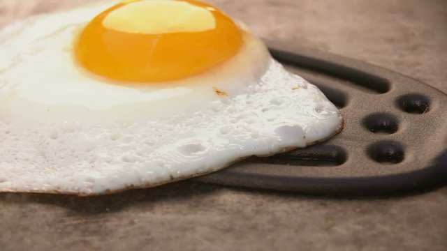 Cook picks up fried egg with a spatula grill