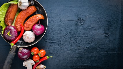 Grilled sausages in a pan with fresh vegetables. Wooden surface. Top view.