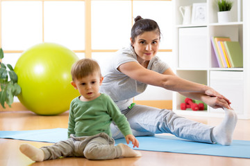 Fototapeta premium Sportive woman is engaged in fitness and yoga at home. Her son kid by near sitting and playing.