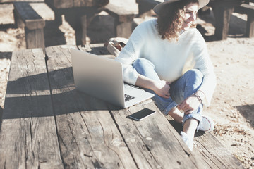 Female traveler sitting at picnic table with mobile phone and laptop. Intentional overexposed,...