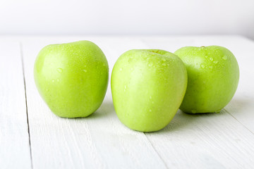Three wet green apples on white wooden background. Close up