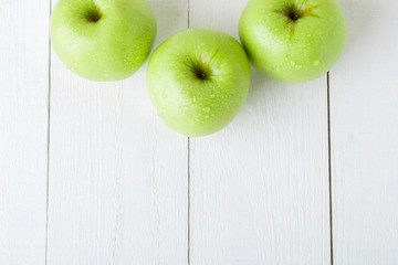 Three wet green apples on white wooden background. Copy space. Top view