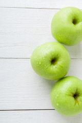 Three wet green apples on white wooden background. Copy space. Top view