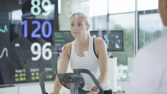  Female athlete on exercise bike being tested and monitored by sports scientist. 