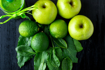 Fototapeta na wymiar Green smoothie near ingredients for it on black wooden background. Apple, lime, spinach, kiwi. Detox. Healthy drink