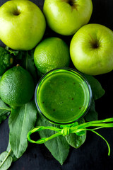Green smoothie near ingredients for it on black wooden background. Apple, lime, spinach. Detox. Healthy drink. Top view