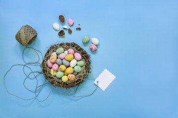 Small painted chocolate eggs in a basket nest with tag on a blue background.