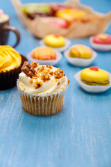 Cupcakes with buttercream and macaroons. Almond macaron cookies. Sweet dessert cakes. On wooden table.