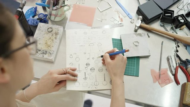 Overhead view looking down jewelry designer in studio sketching out designs. 