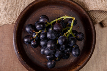 Dark grapes bunch. Ripe grape fruit on rustic plate. On wooden background.