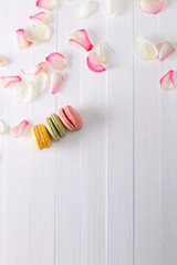 Macaroon cakes with pink rose petals. Different types of macaron. Colorful almond cookies. On white wooden rustic background.