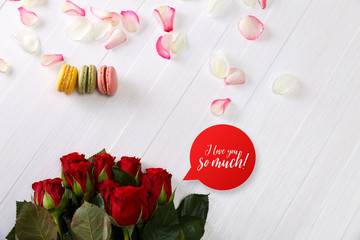 Macaroon cakes with bouquet of red roses. Different types of macaron. I love you speech bubble. White wooden rustic background.