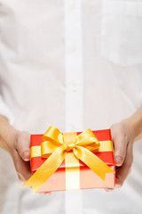 Male hands holding a gift box. Present wrapped with ribbon and bow. Christmas or birthday red package. Man in white shirt.