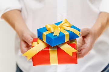 Male hands holding a gift boxes. Present wrapped with ribbon and bow. Christmas or birthday red, blue package. Man in white shirt.