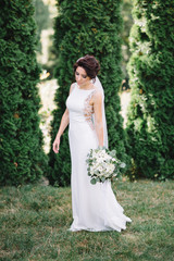 Bride in elegant gown holds hand with bouquet down standing on the lawn