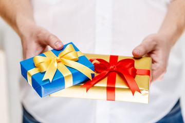 Male hands holding a gift boxes. Presents wrapped with ribbon and bow. Christmas or birthday blue, golden packages. Man in white shirt.