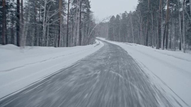 Personal Perspective Shot Of Driving Along Snowbound Empty Road Surrounded By Trees 