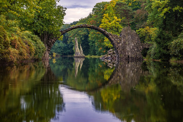 Fototapeta na wymiar Autumn, cloudy evening over Devil's bridge in the park Kromlau, Germany