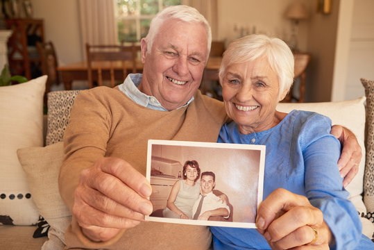 Smiling senior couple holding a photo of their youthful selves 