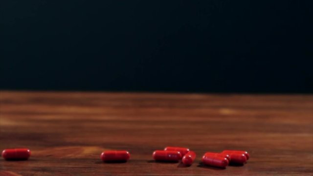 Girl's hand pouring red pils on woden table, slow motion hd video