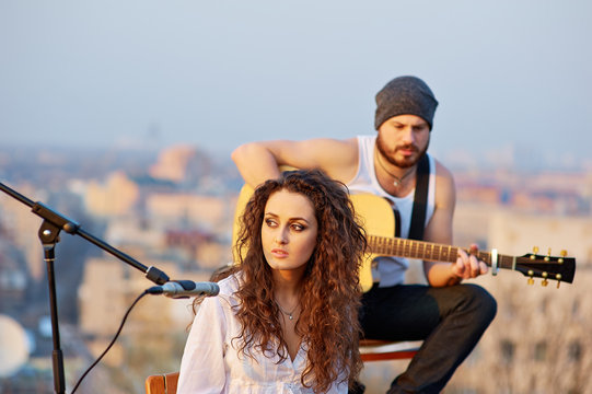 Young beautiful girl singing with a guitar player outdoors