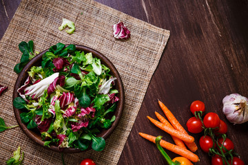 Provence salad. Leaves of endive or chicory, lamb and rose salad. Cherry tomatoes and carrot. Raw vegetables. On wooden table.