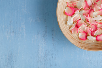 Petals of white and pink roses on blue painted rustic background. Fresh natural flowers in bowl. Dirty grunge wooden board.