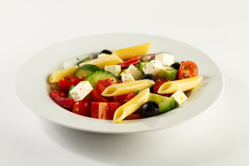 Tasty beautiful greek traditional greek or italian salad with vegetables and pasta on plate. Bright Background.