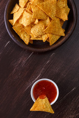 Nachos chips. Delicious salty tortilla with sweet salsa or chilli sauce on wooden background. Snack on rustic plate.