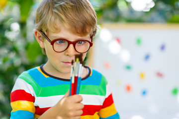 Little kid boy with glasses holding school equipment