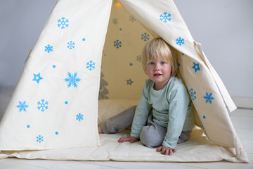 child with fluffy white hair and blue eyes sits inside a snowflake decorated tipi