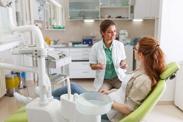 A professional female dentist, equipped with a bright smile, converses with her red hair female...