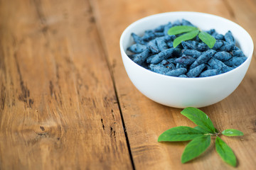 Ripe honeysuckle (lonicera) in the bowl on a wooden table.