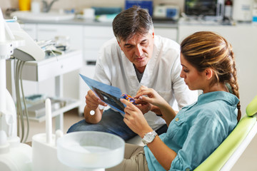 Senior male dentist in dental office talking with female patient and preparing for...