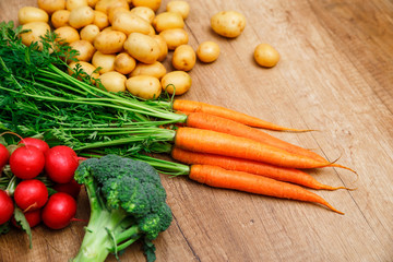 Potatoes with carrot. Red radish, brocoli and raw new potato. Fresh natural vegetables. Organic bio food. On wooden table.
