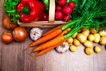 Vegetables. Potatoes, carrot and red pepper. Lettuce salad, garlic and brocoli. Onion and radish. Wooden basket on rustic table.