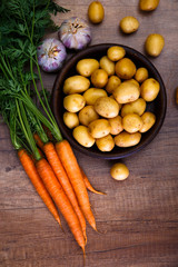 Potatoes in a rustic plate. Carrot, garlic and raw new potato. Fresh natural vegetables. Organic bio food on wooden table.