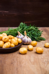 Potatoes in plate. Carrot tops, garlic and raw new potato. Fresh natural vegetables. Organic bio food on rustic wooden table.