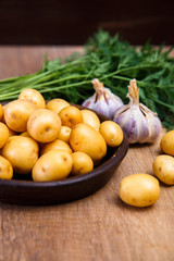 Potatoes in plate. Carrot, garlic and raw new potato. Fresh natural vegetables. Organic bio food on rustic wooden table.