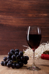 Red wine. Bottle and Wineglass with dark grapes branch. On rustic wooden background.