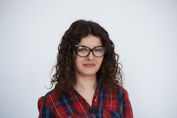 Young attractive smiling Curly hair programmer woman in trendy glasses dressed in check shirt look to the camera. Talented manager with long hair portrait on neutral background feel good.