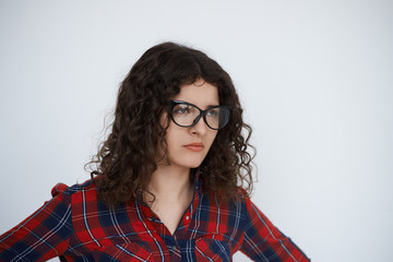 Stylish dressed brunette woman look away on neutral white background. Close up portrait of serious female.Curly hair Girl ready to scold somebody. Unhappy emotion on the face.