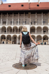 A woman in a blue T-shirt with a backpack on her back is standing in the courtyard of the Wawel Castle in Cracow and enjoying the architecture of the building. Poland. Renaissance.