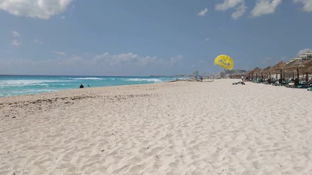 Beautiful sandy beach with a turquoise ocean. Yellow parasail is tied up in the distance.