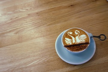 Coffee in a blue cup on wooden table. Cappuccino with swan latte art pattern