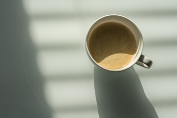 Cup of coffee on the white glass table. Reflections and shadows. Conceptual modern office.