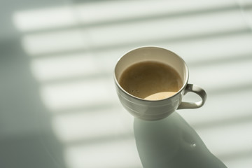 Cup of coffee on the white glass table. Reflections and shadows. Conceptual modern office.