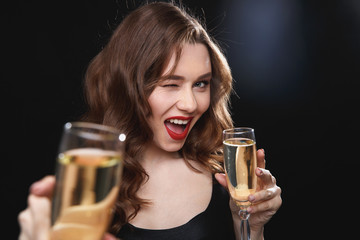 Cheerful young woman giving you glass of champagne and winking