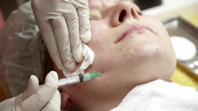 Beautician making anti aging injections to the cheek for the woman closeup