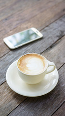 Hot coffee and smartphone on a wooden table.
